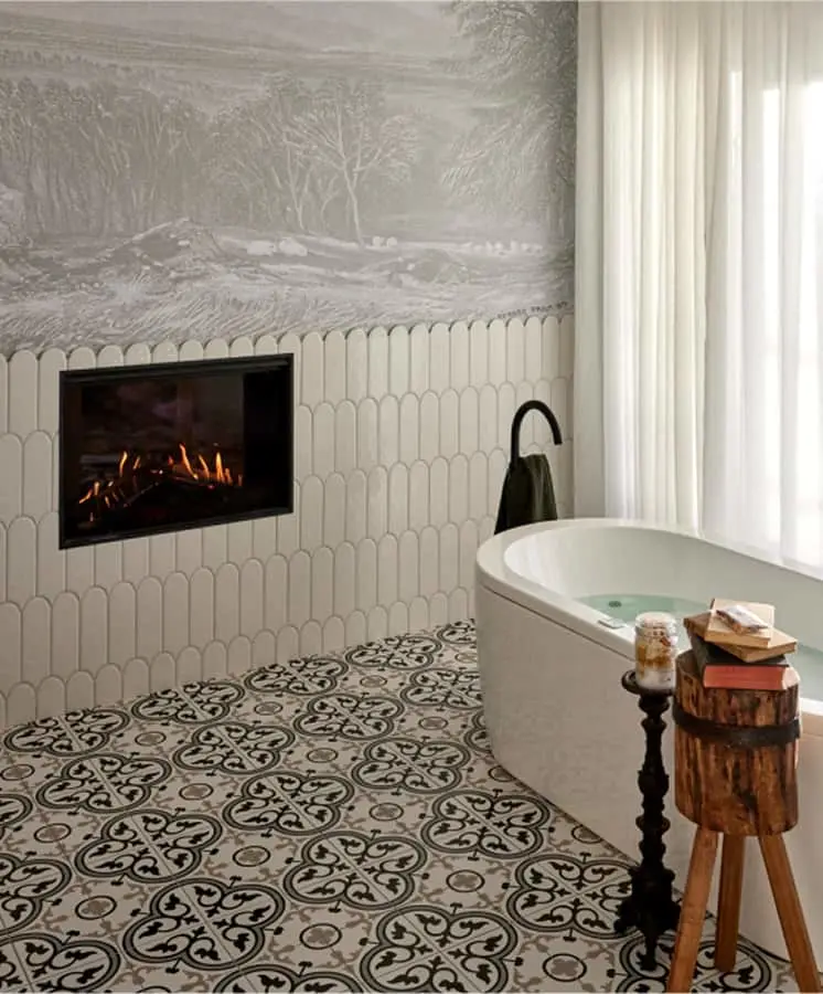 Elegant bathroom with built-in fireplace, white tub, patterned floor tiles, and decorative wall mural above tile wainscoting.