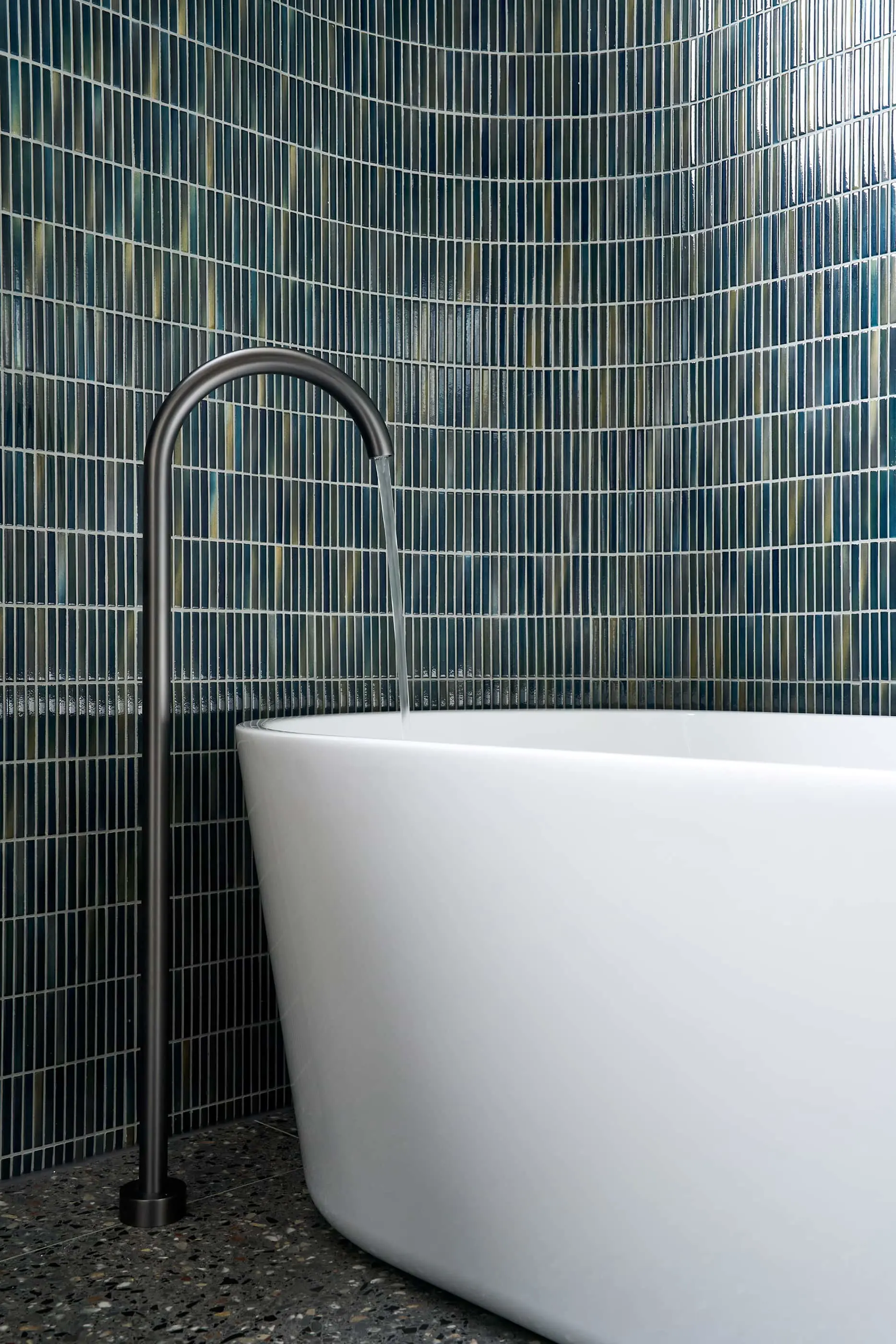 Modern bathroom with white freestanding bathtub, black curved faucet, and blue-green mosaic tile wall.