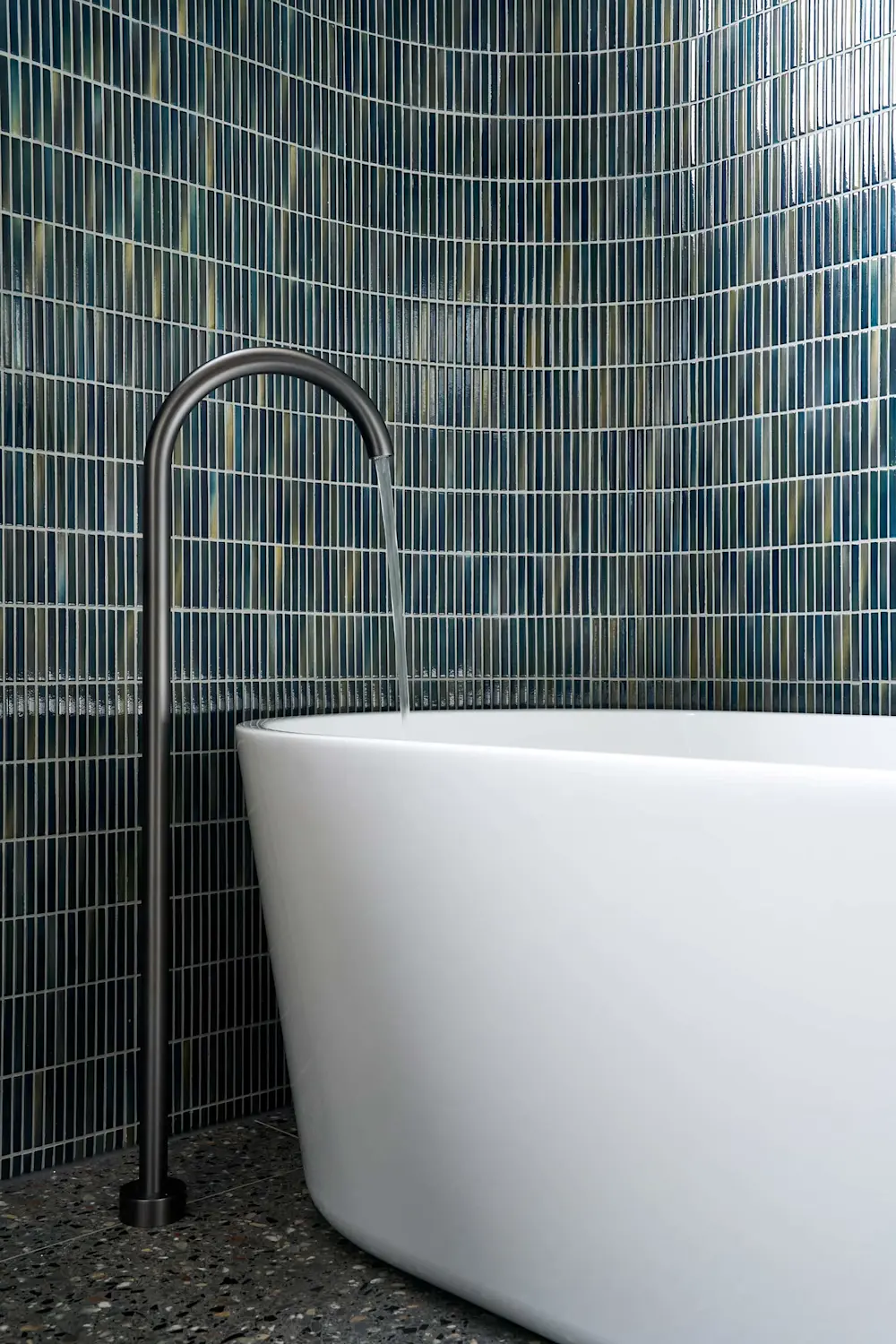 Modern bathroom with white freestanding bathtub, black curved faucet, and blue-green mosaic tile wall.