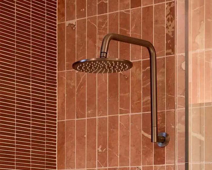 Bronze rainfall showerhead mounted on brown tiled bathroom wall with glass shower door visible on right side.
