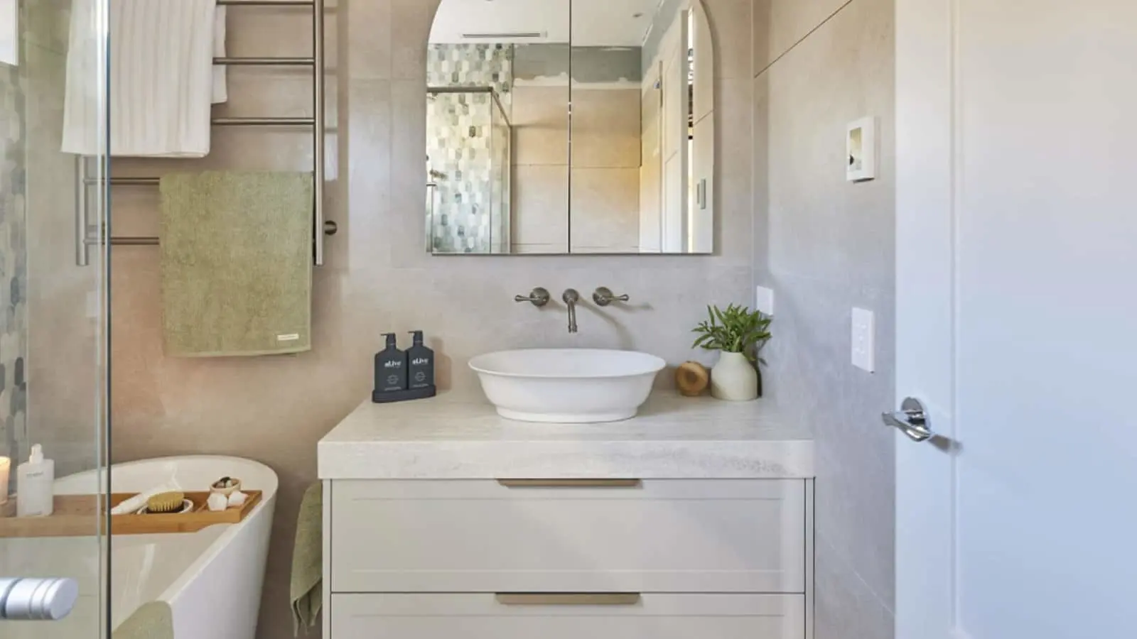 Modern bathroom with white vessel sink, wall-mounted faucet, mirror cabinet, and partial view of bathtub with glass partition.