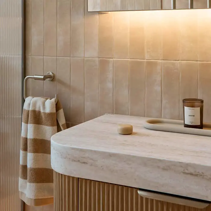 Modern bathroom with beige tiled walls, marble countertop, striped towel on rack, and candle on sink surface.