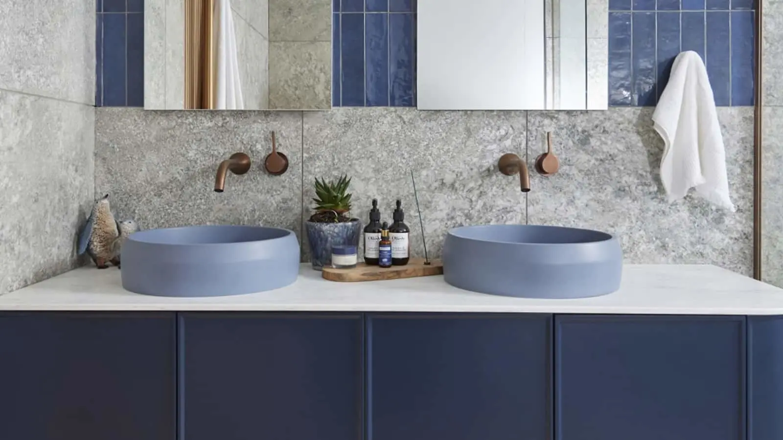 Modern bathroom with dual blue vessel sinks, copper wall-mounted faucets, marble backsplash, and navy blue cabinetry.
