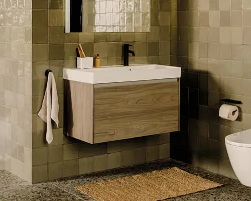 Modern bathroom with wall-mounted wood vanity, white sink, beige tiled walls, mirror, towel hook, and bath mat on floor.