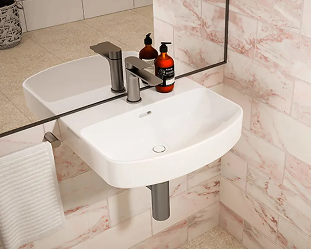 Modern white wall-mounted bathroom sink with metal faucet and two amber soap dispensers against pink marble tiles.