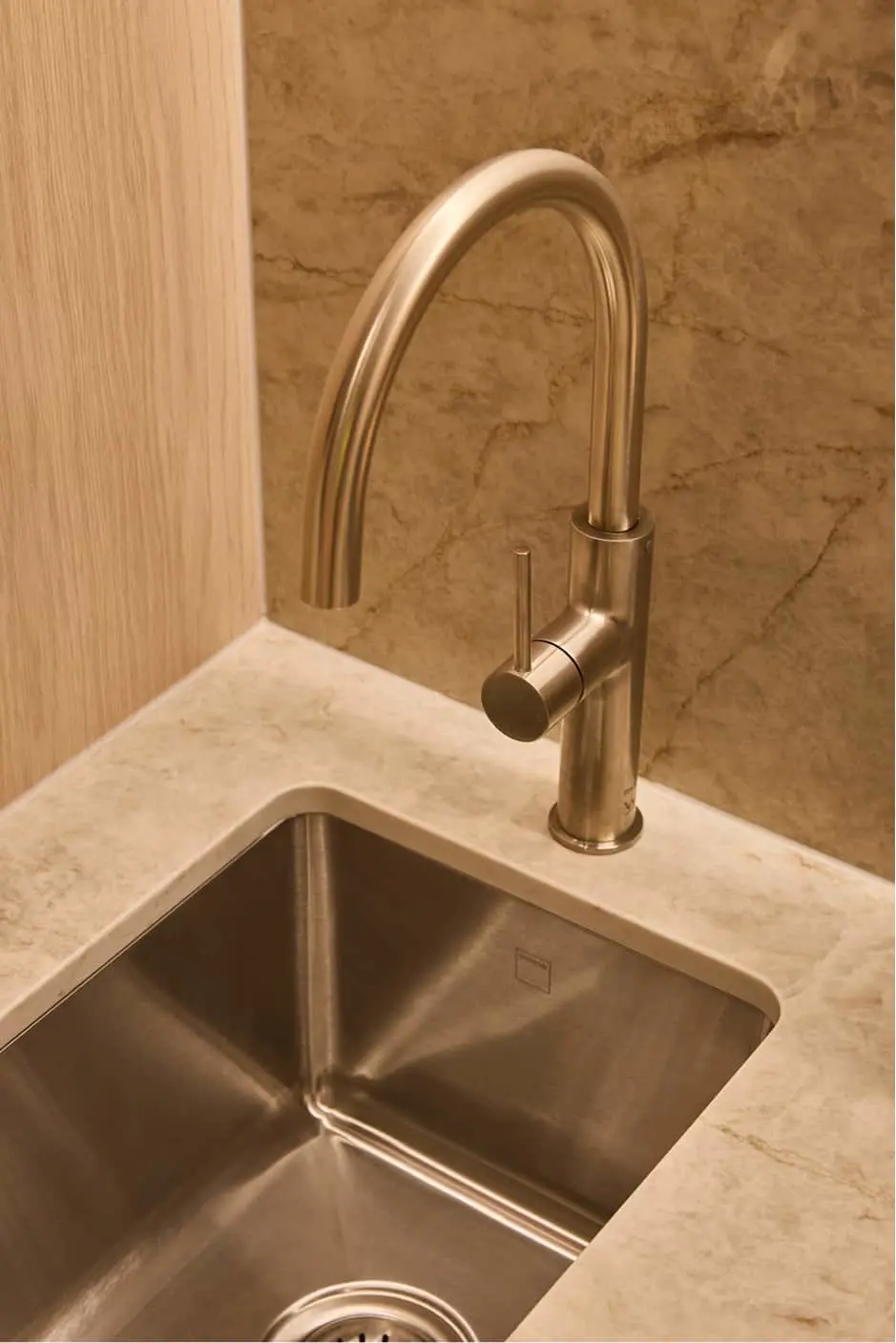 Brushed metal kitchen faucet with curved spout and single handle mounted on white countertop with stainless sink.