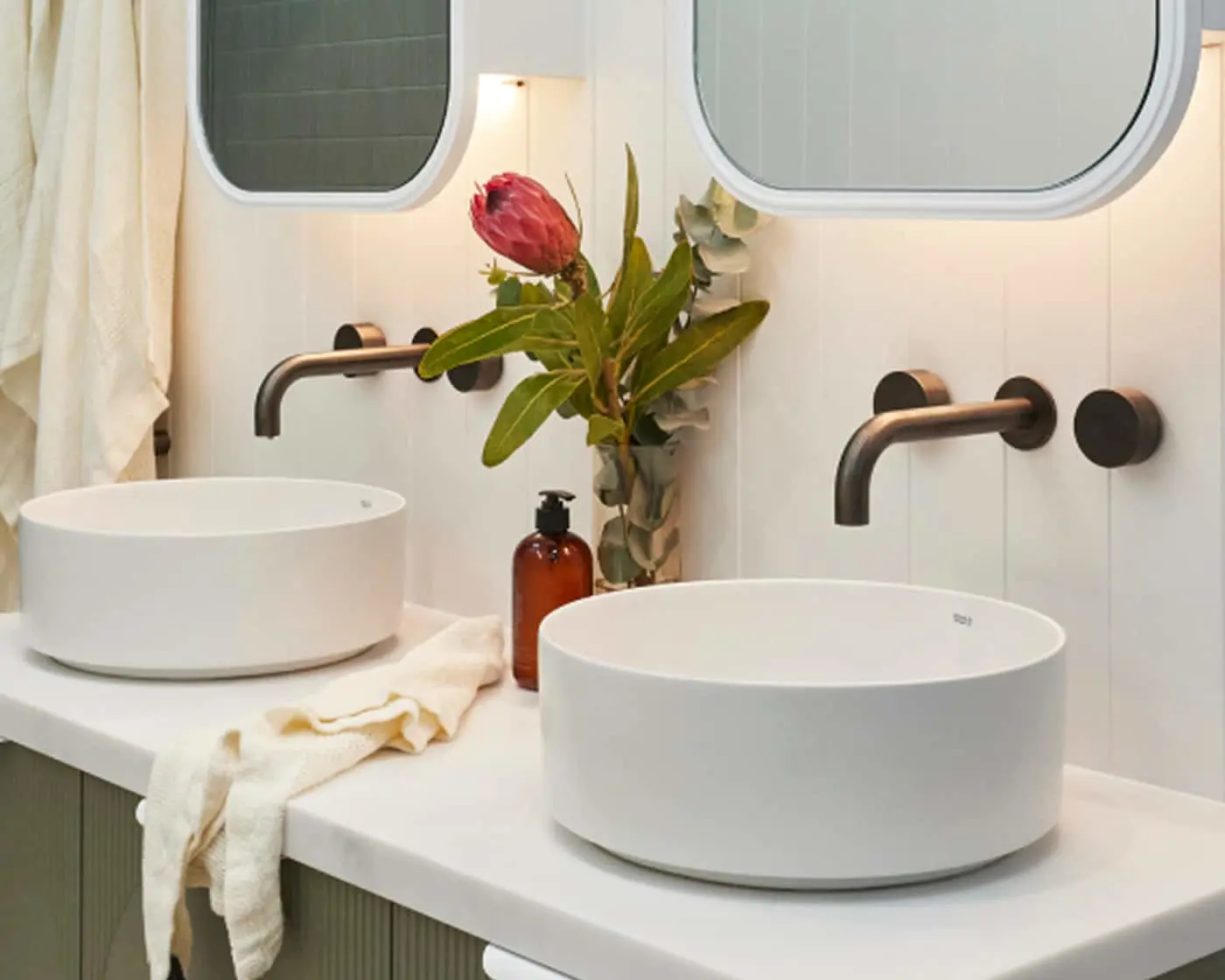 Modern bathroom with two white vessel sinks, black wall-mounted faucets, and a red protea flower in a vase.