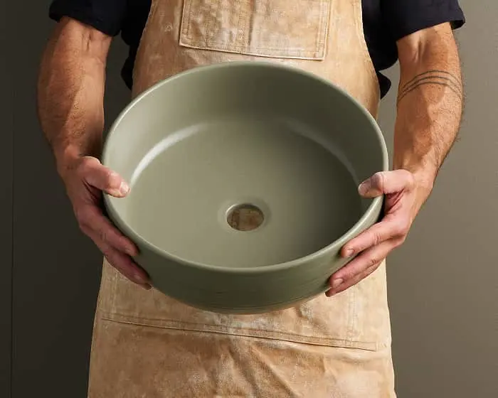 Person wearing beige apron holding a light green ceramic vessel with a hole in the center.