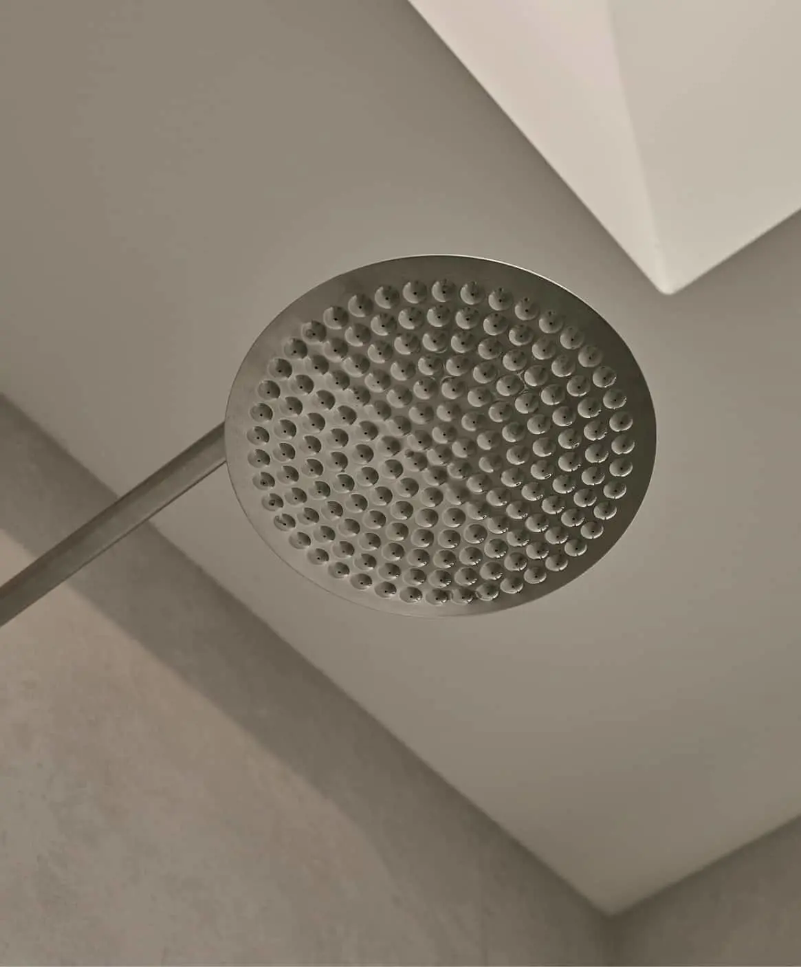 Round stainless steel rainfall shower head mounted on ceiling in a minimalist bathroom.