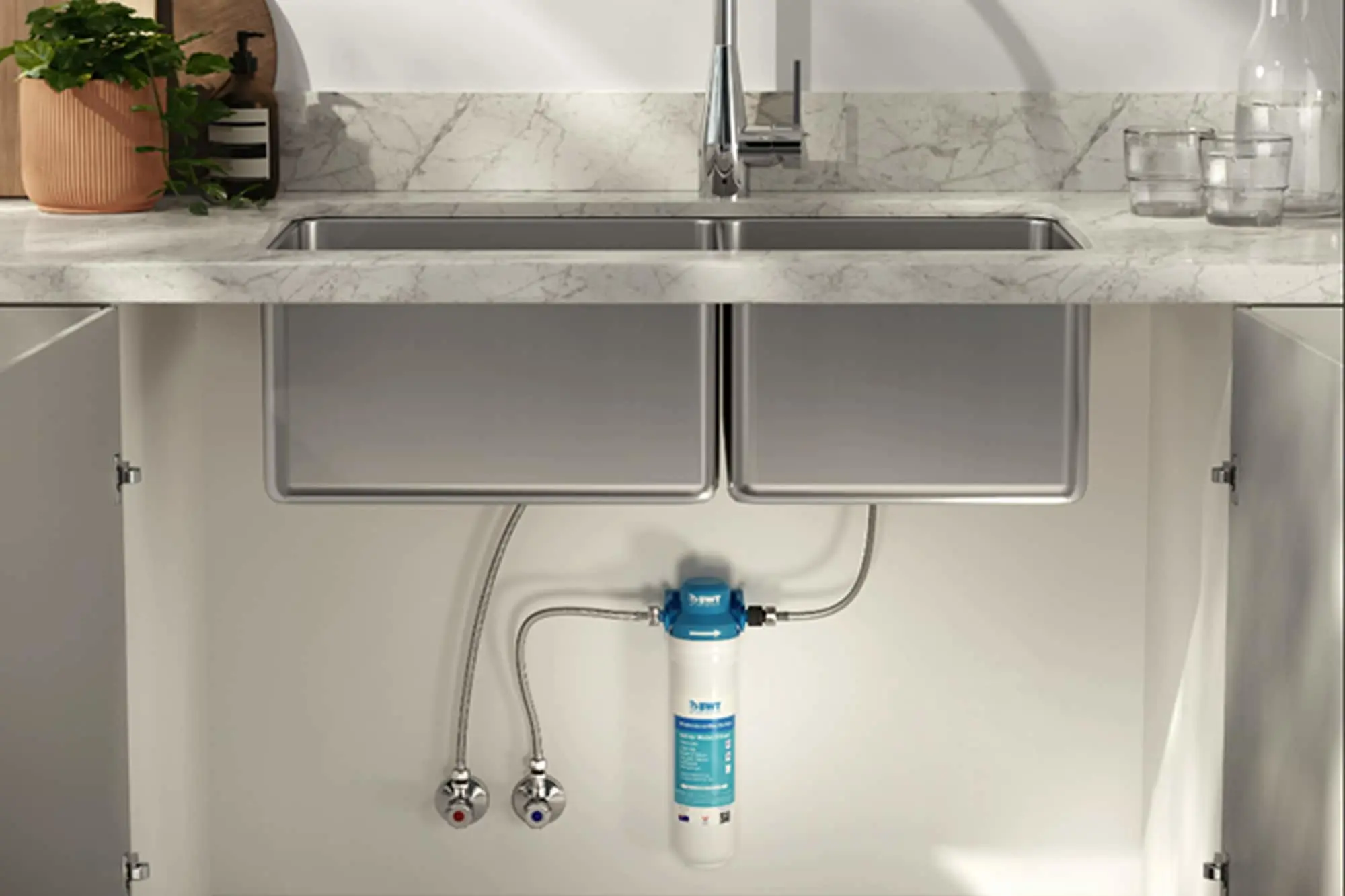 Modern kitchen sink with under-counter water filtration system installed, marble countertop, and potted plant.