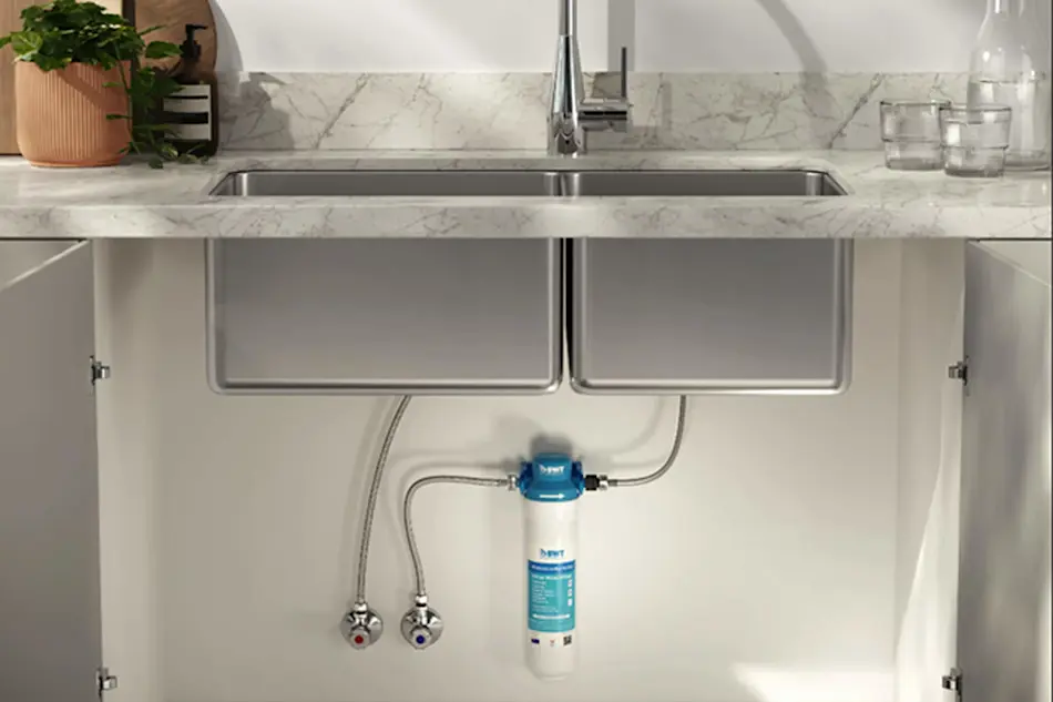 Modern kitchen sink with under-counter water filtration system installed, marble countertop, and potted plant.