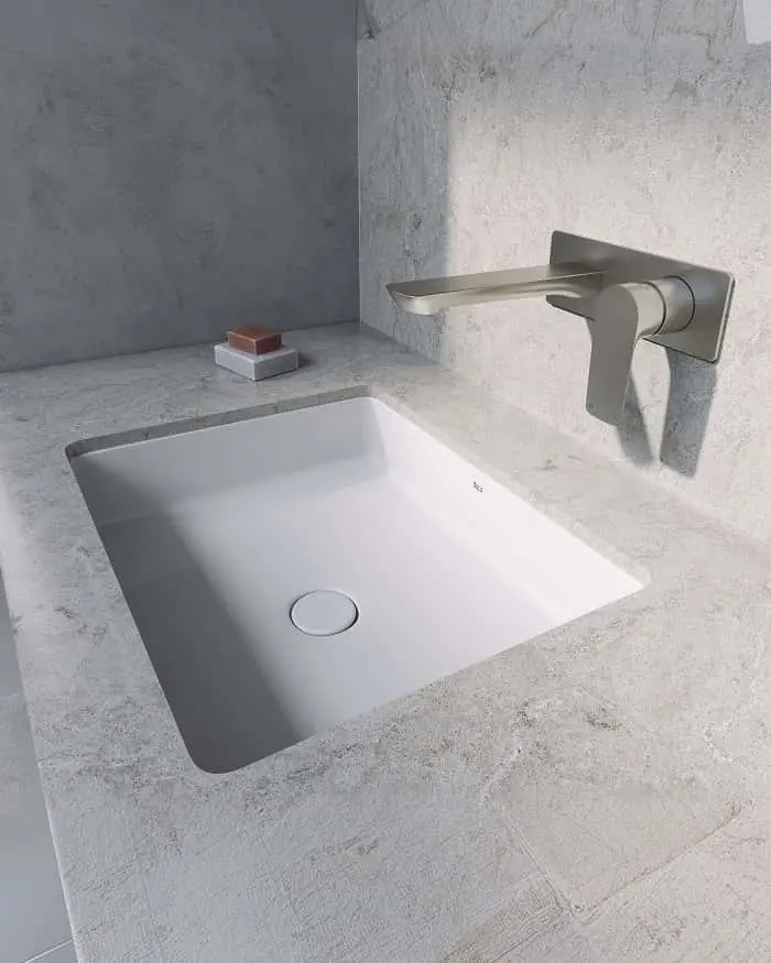 White rectangular undermount sink with brushed nickel wall-mounted faucet on concrete countertop and walls.