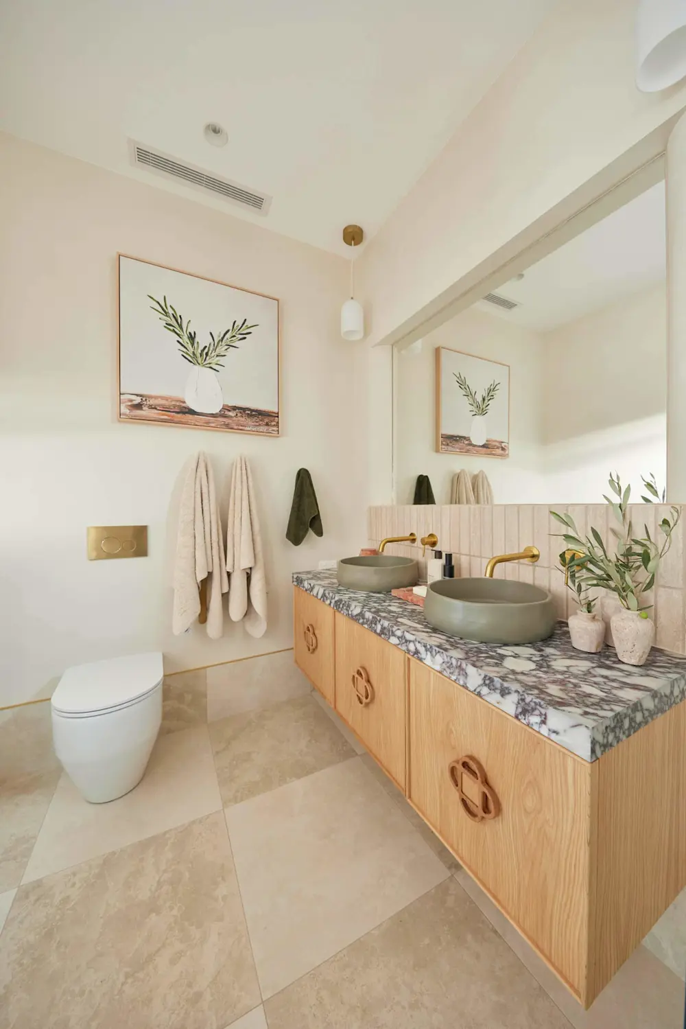 Modern bathroom with wooden vanity, dual sage vessel sinks, marble countertop, white toilet, and botanical artwork.