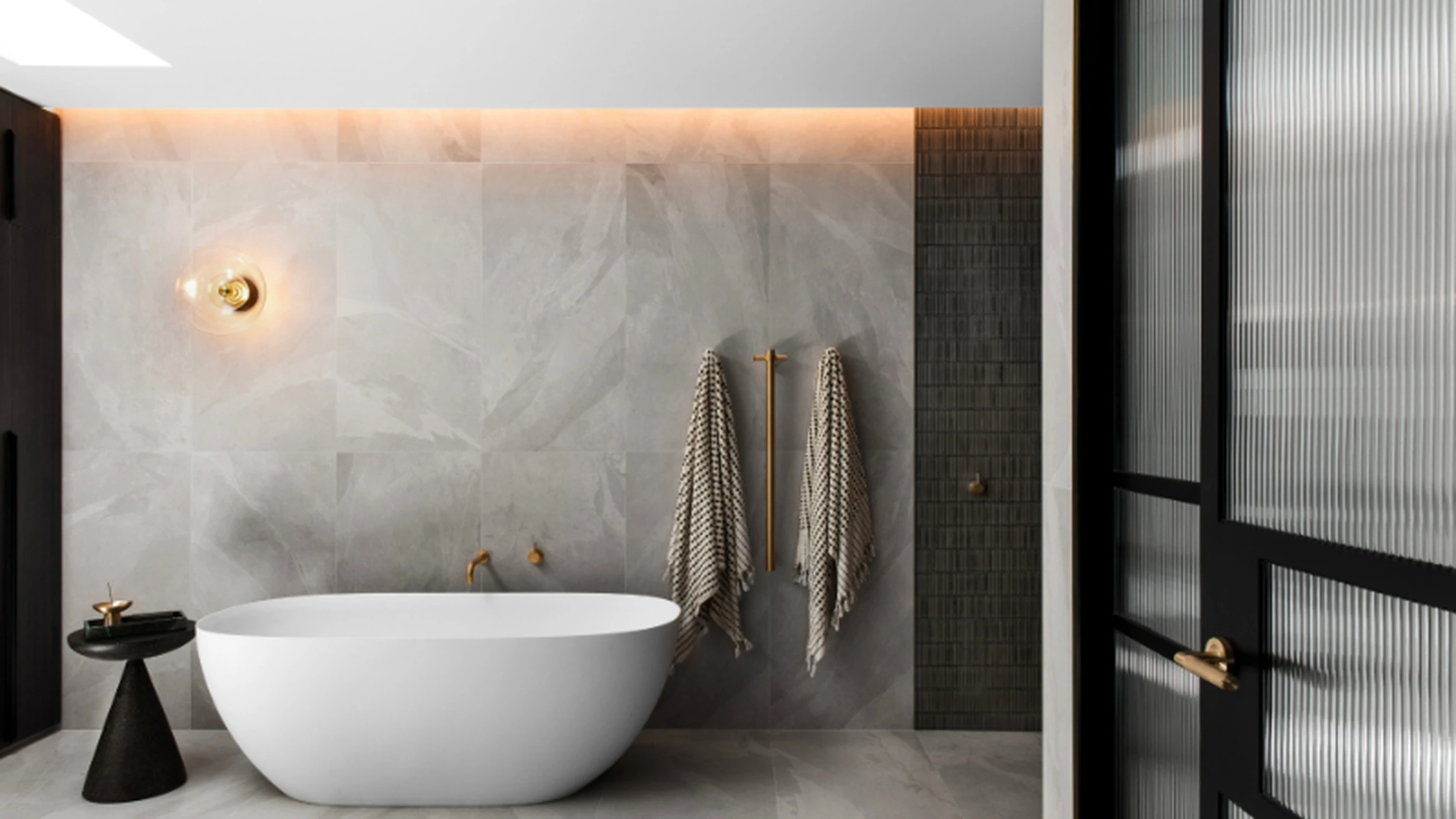Modern bathroom with white freestanding tub, marble walls, striped towels, brass fixtures, and black side table.