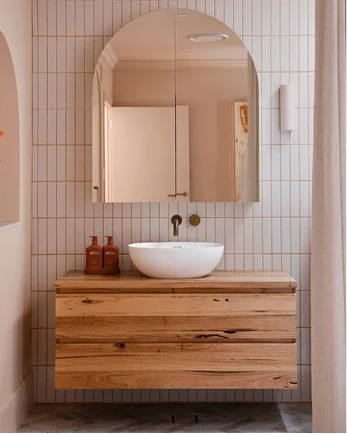 Modern bathroom with arched mirror, white vessel sink on wooden vanity, and vertical tiled walls.