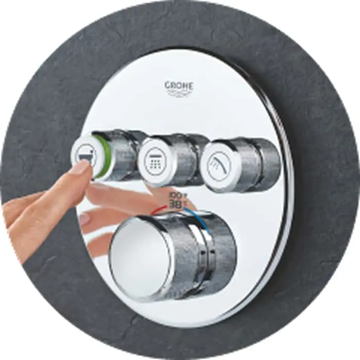 Hand pressing a button on a circular GROHE shower control panel with multiple chrome dials and temperature indicator.