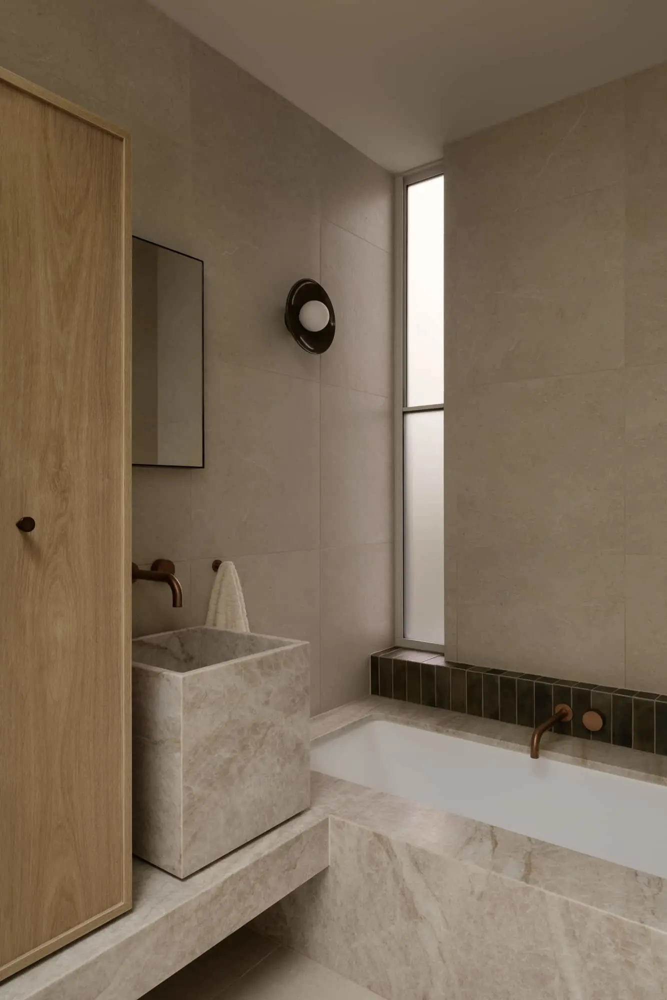 Modern minimalist bathroom with stone sink, wooden door, white bathtub, and tall window in neutral beige tones.