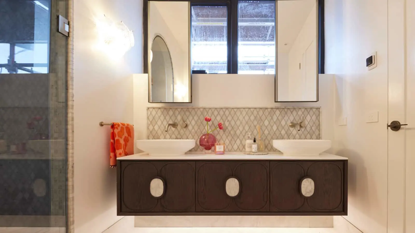 Modern bathroom with double vessel sinks on dark wood vanity, diamond-pattern backsplash, and orange towel.