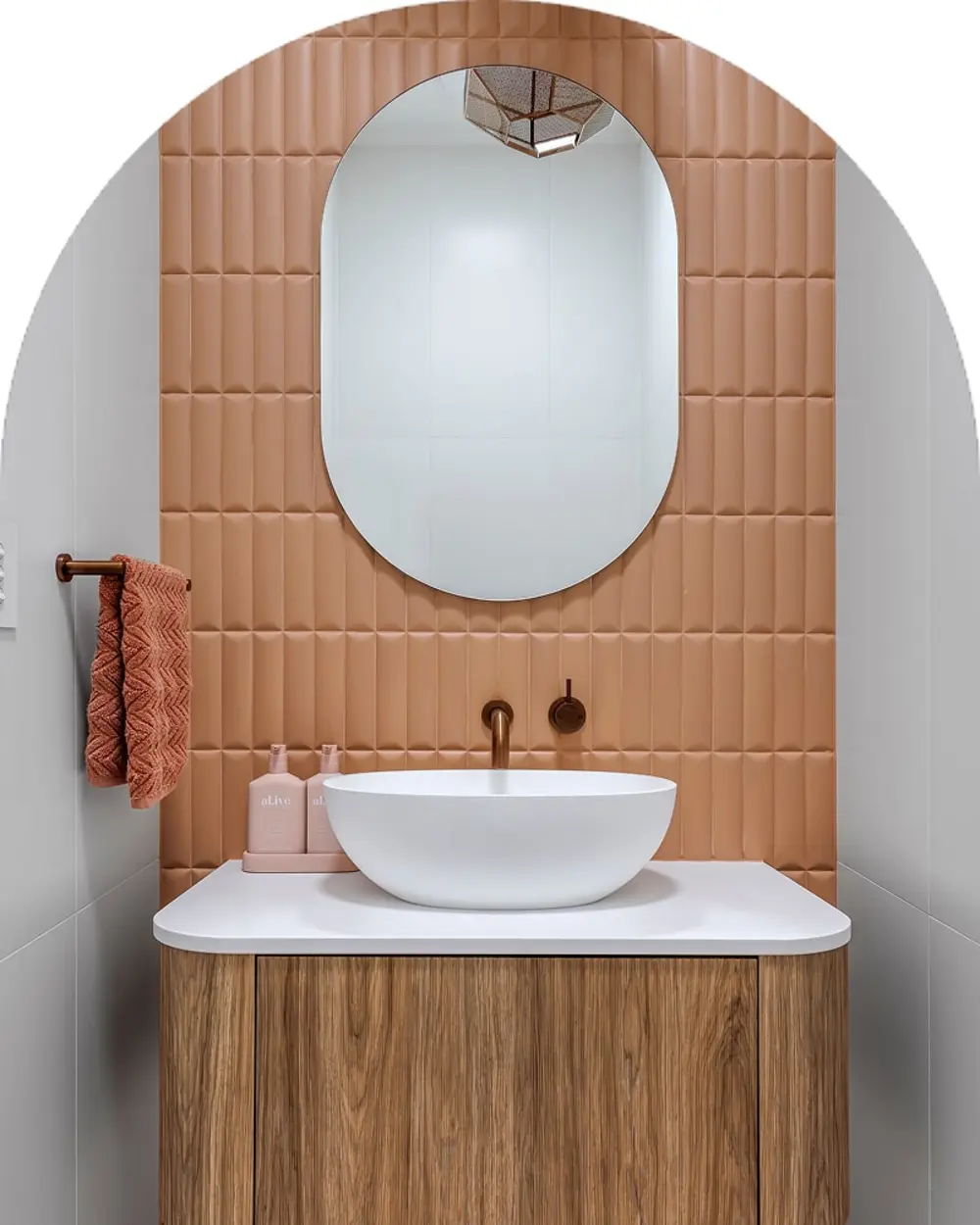 Modern bathroom with peach tile wall, oval mirror, white vessel sink on wooden vanity, and coral towel on side rack.