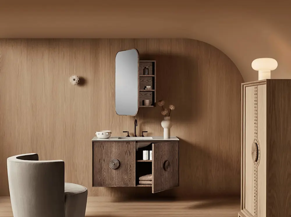 Modern bathroom with wooden vanity, rounded mirror, and beige walls. Gray chair in foreground and cabinet to the right.