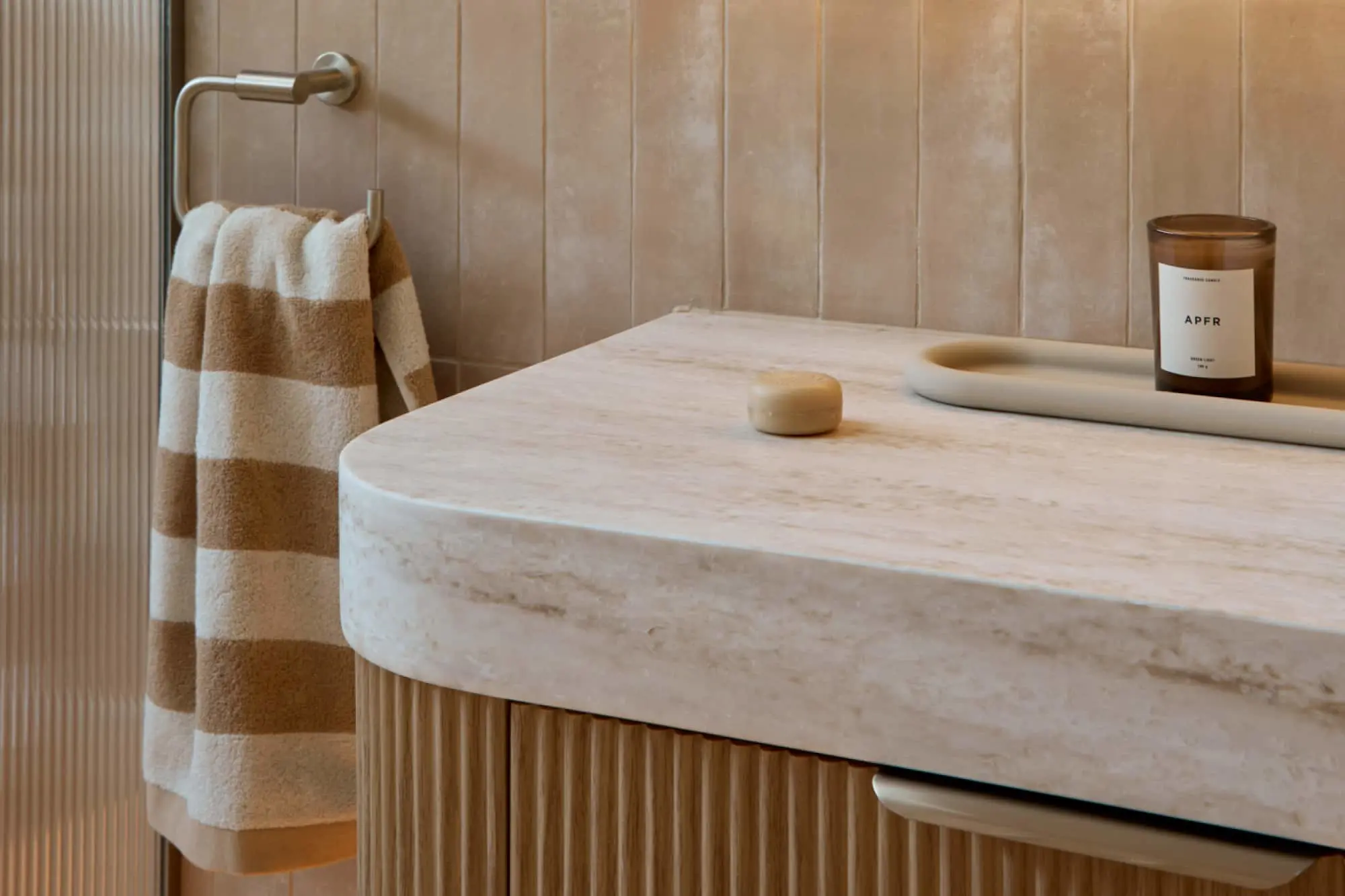 Marble bathroom countertop with candle and soap dish, striped brown and white towel hanging on wall-mounted holder.