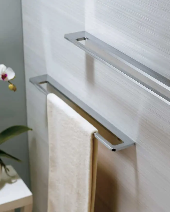 Modern stainless steel towel bars mounted on a light-colored bathroom wall, with a white towel hanging and small orchid visible.