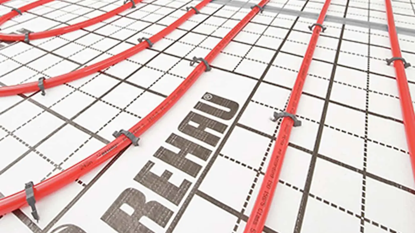 Red underfloor heating pipes installed on a grid mesh with Rehau branding visible on the installation surface.