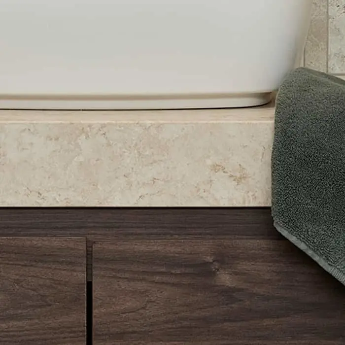 Corner of a bathroom showing white basin on beige stone base with dark wood vanity and green towel.