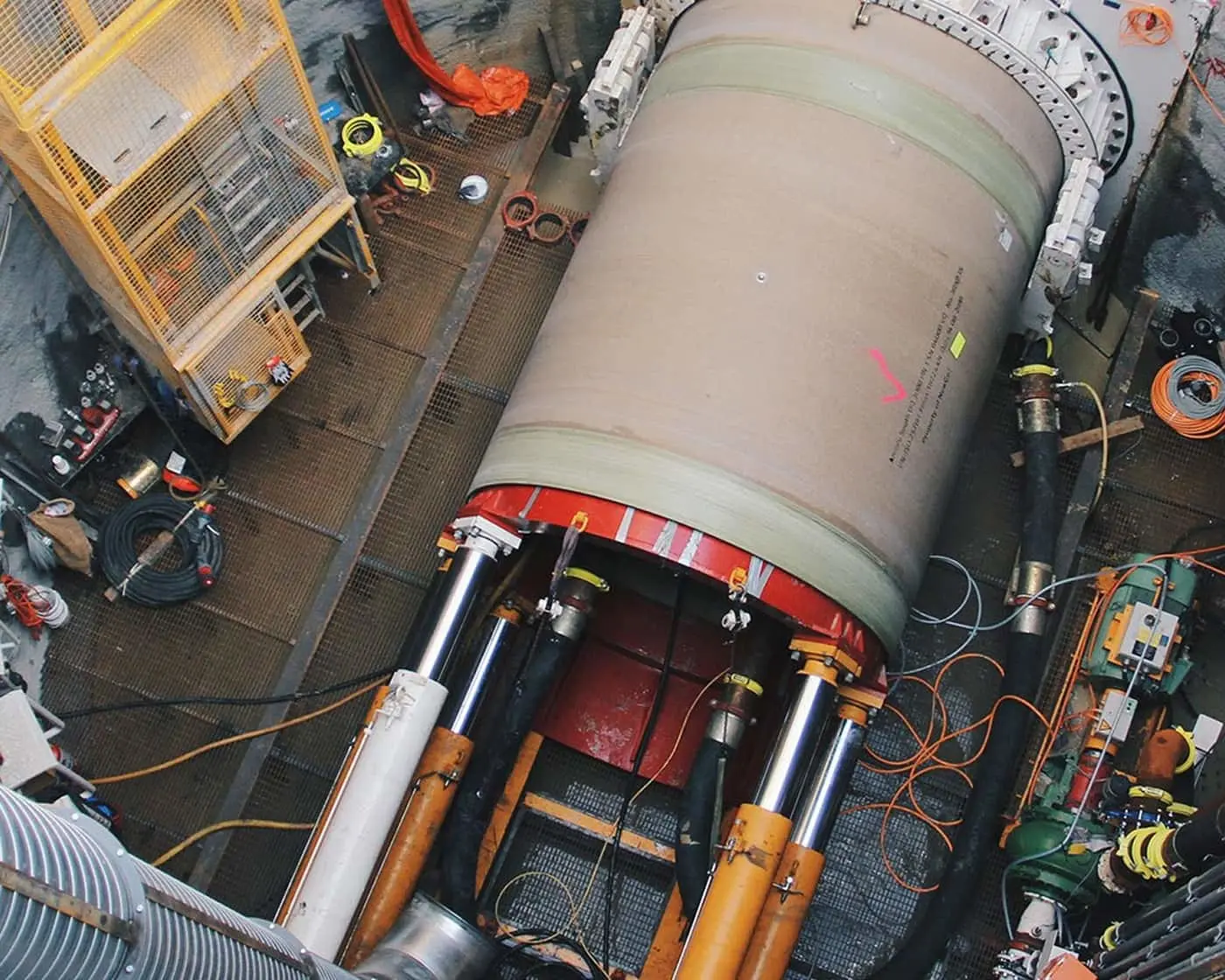 Aerial view of a large cylindrical tunnel boring machine component with hydraulic supports in an underground construction site.
