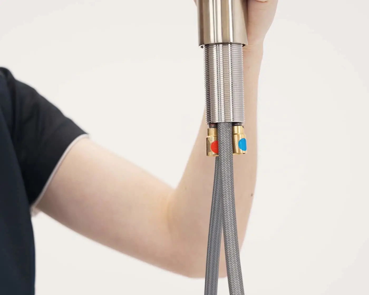 Person holding a tap with braided hoses and color-coded connectors against white background.