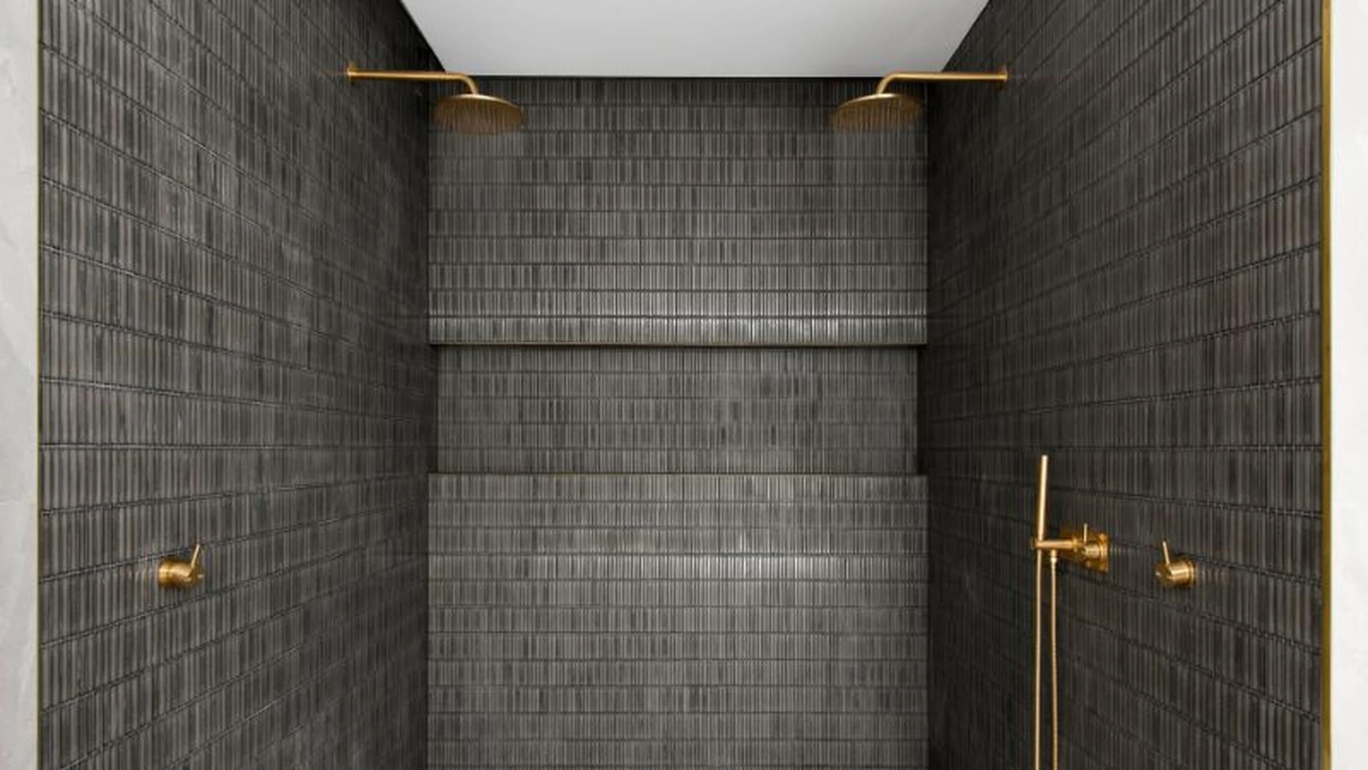 Modern shower with dark gray tiled walls, gold fixtures, and dual rainfall showerheads mounted on brass pipes.