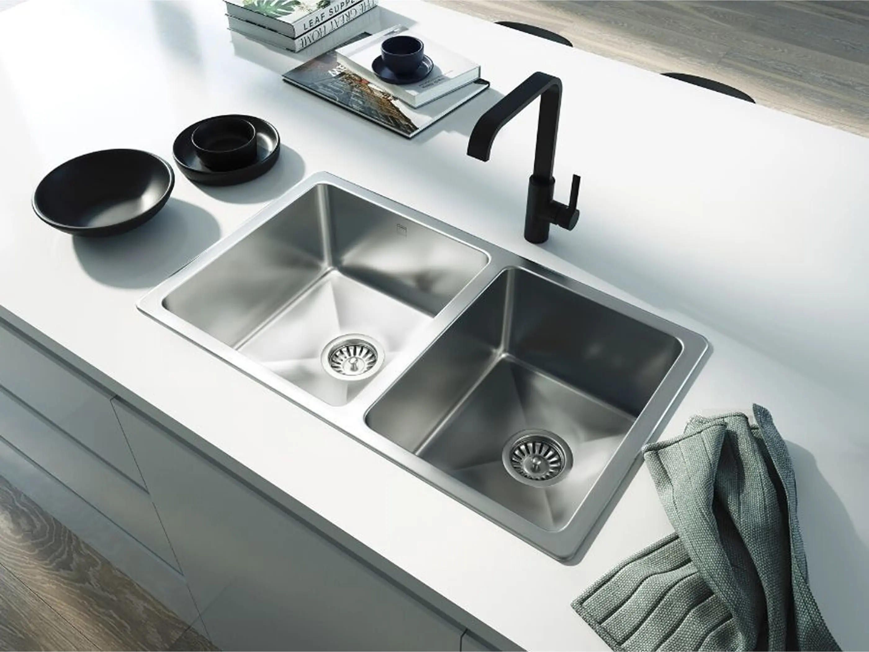 Modern kitchen with double stainless steel sink, black faucet, black dishware, and decorative books on white countertop.