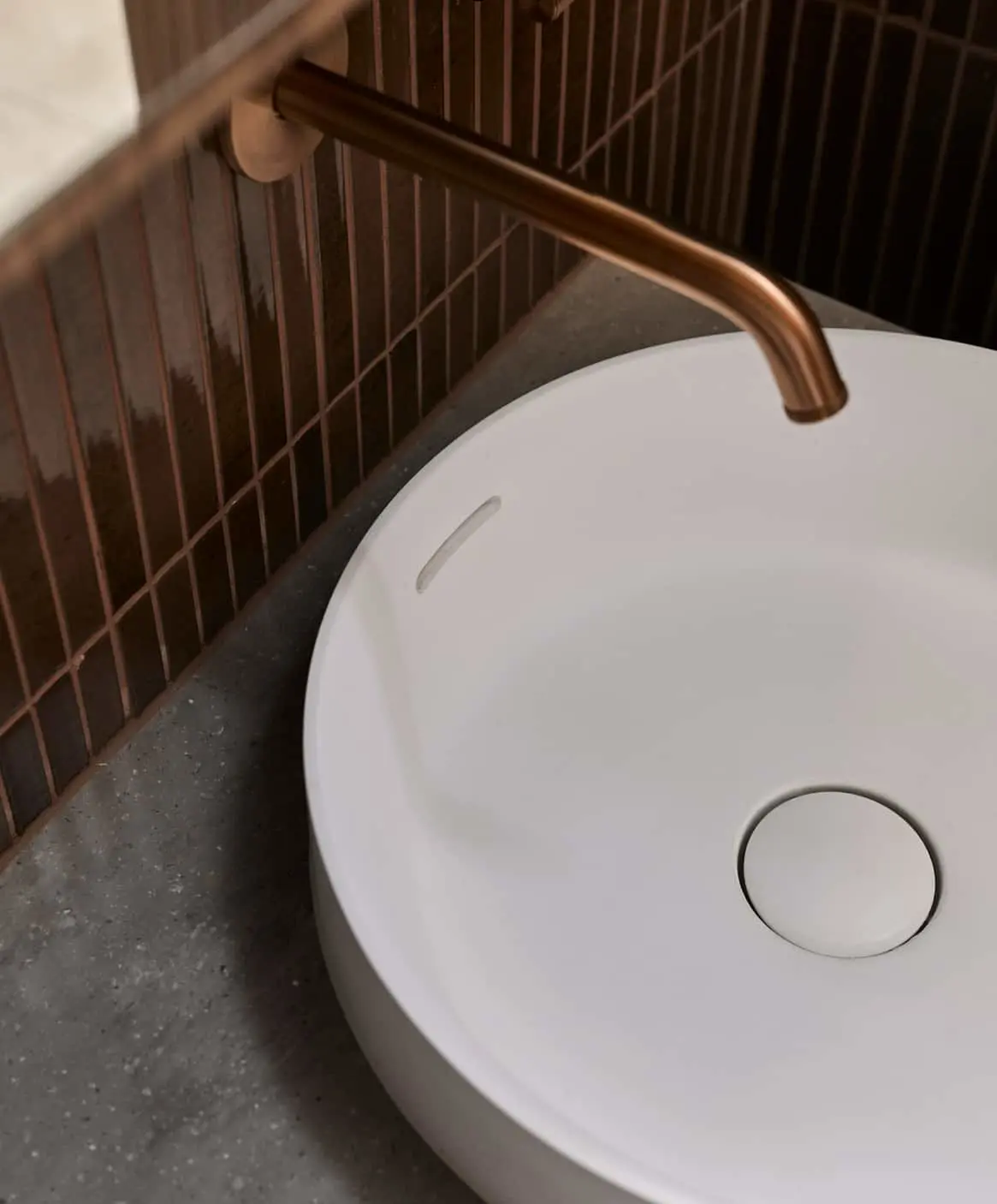 Close-up of modern bathroom fixtures showing white basin with bronze faucet.
