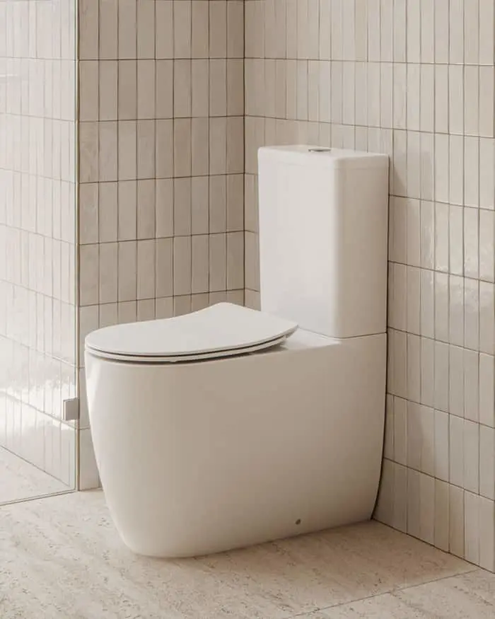 Modern white toilet with closed lid in a bathroom with beige tiled walls and light floor.