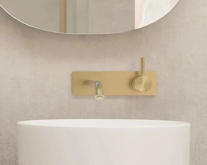 Modern bathroom with white oval sink, gold wall-mounted faucet and control panel, and circular mirror above.
