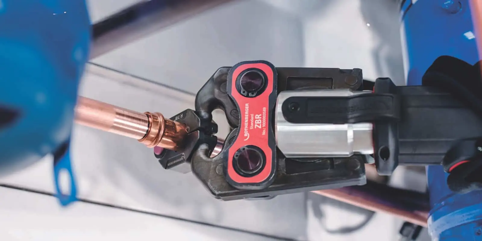 Red and black plumbing press tool clamping a copper pipe.