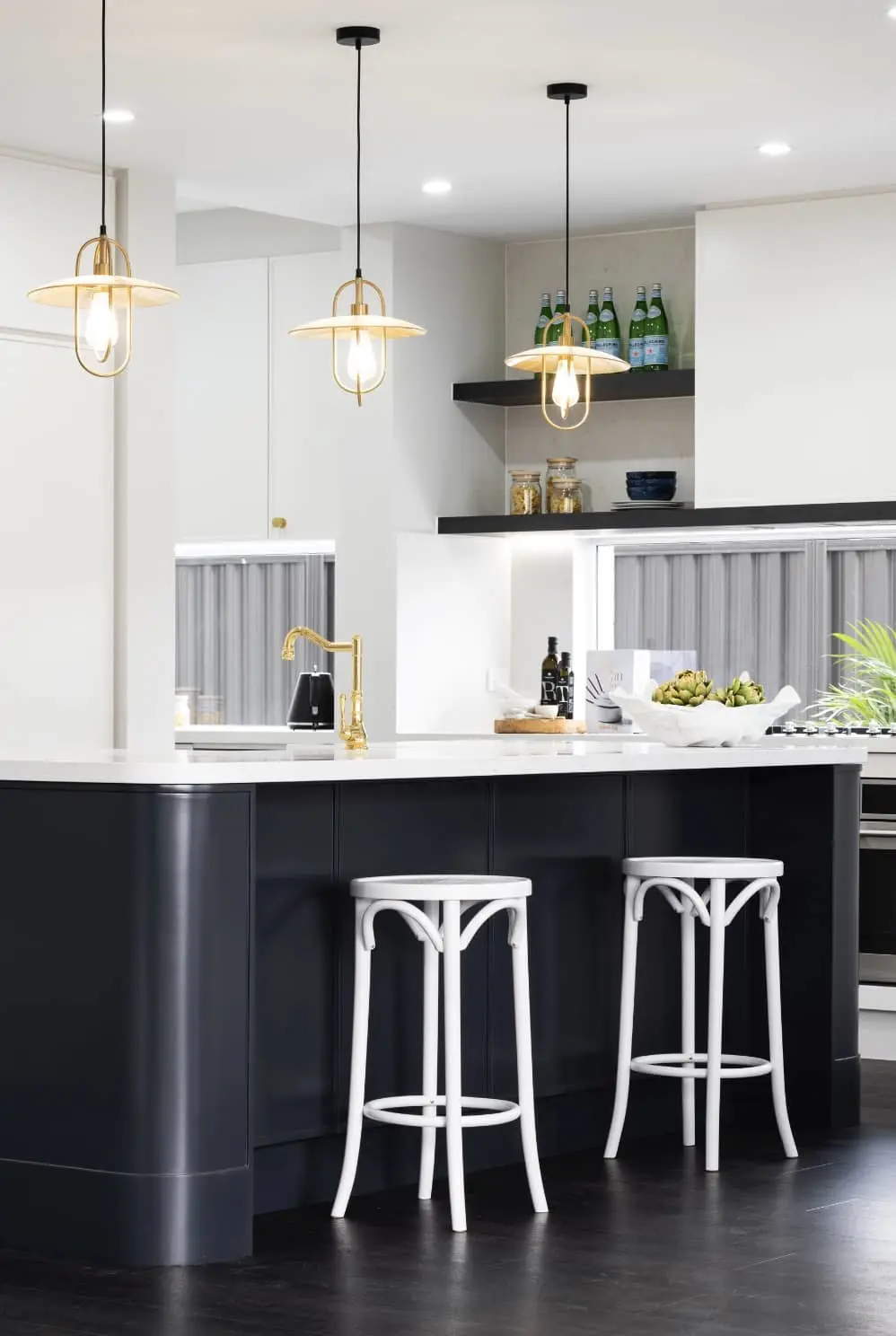 Modern kitchen with navy island, white countertops, gold pendant lights, and white bar stools.