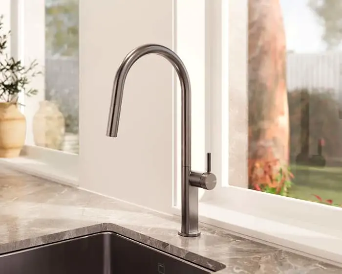 Modern stainless steel kitchen faucet with pull-down sprayer on marble countertop next to window with garden view.
