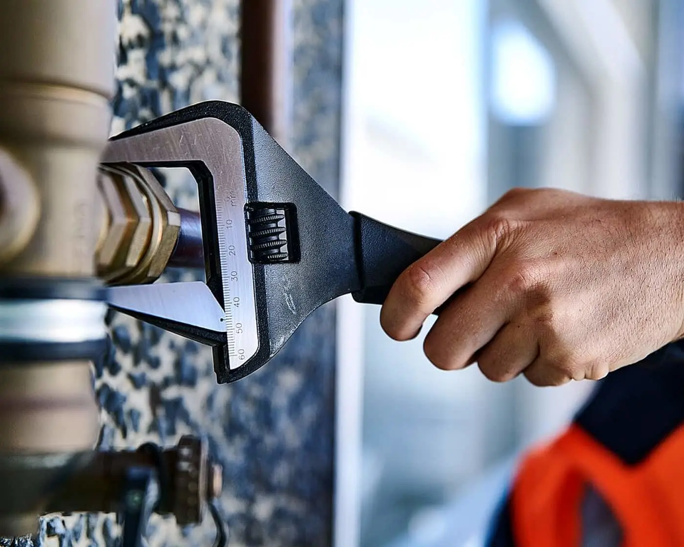 Hand using an adjustable wrench to tighten or loosen a pipe fitting in a plumbing repair.