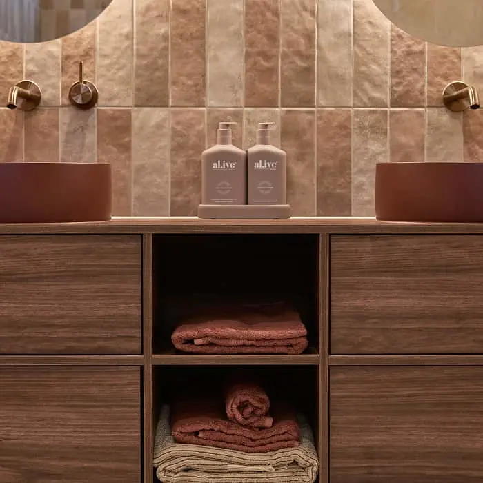 Modern bathroom vanity with wooden cabinets, terracotta sink, beige tiled wall, and neatly folded towels in open shelving.