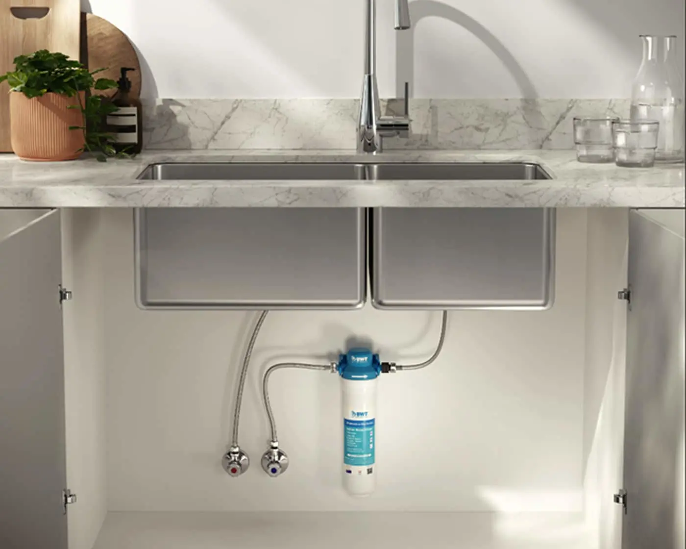 Modern kitchen sink with water filter system installed underneath, marble countertop, and potted plant on the side.