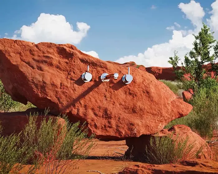 Chrome bathroom faucet mounted on a large red rock formation in a desert landscape with blue sky and white clouds.
