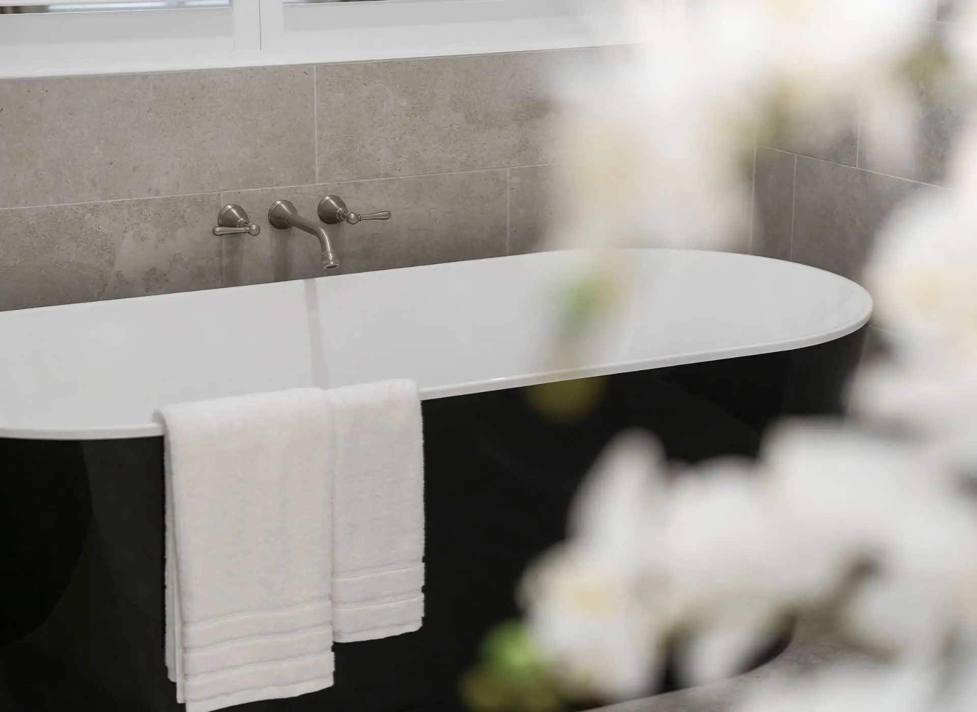 Modern black and white freestanding bathtub with wall-mounted brushed nickel faucet and white towel hanging on the side.