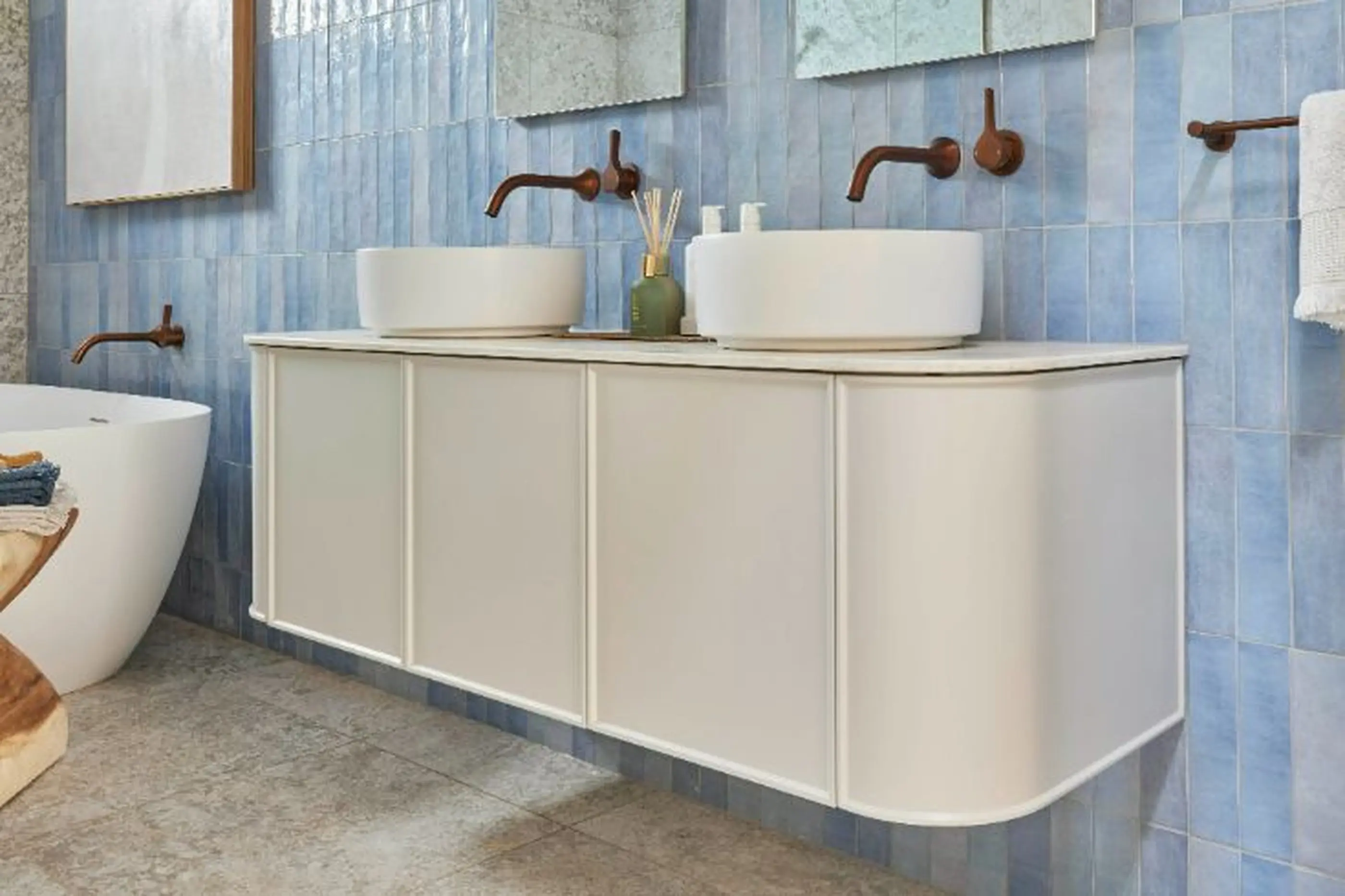 Modern bathroom with white vanity, vessel sinks, copper faucets, and blue vertical tile backsplash.
