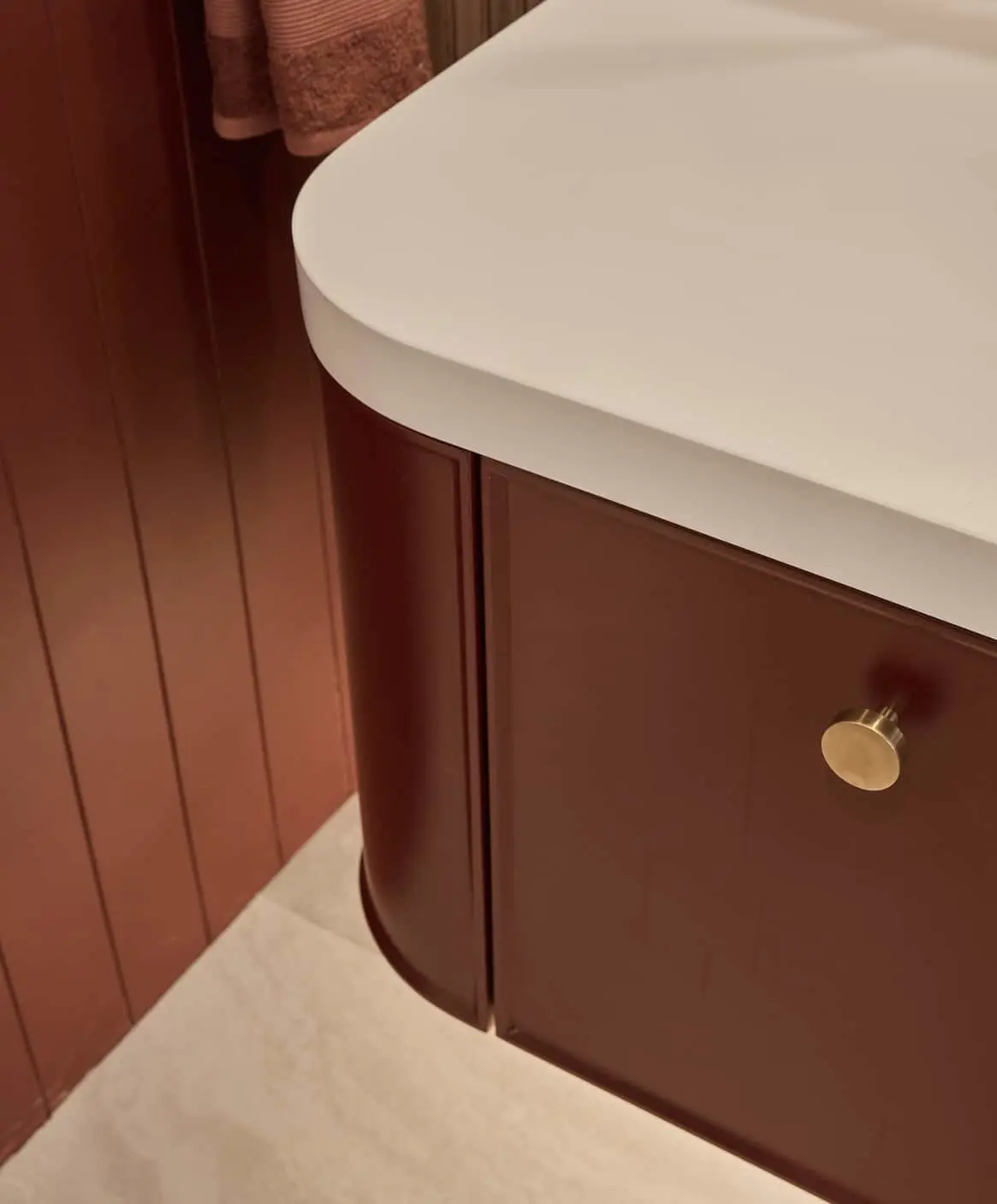 Curved wooden bathroom vanity with white countertop, brass knob, and matching wood paneled wall.