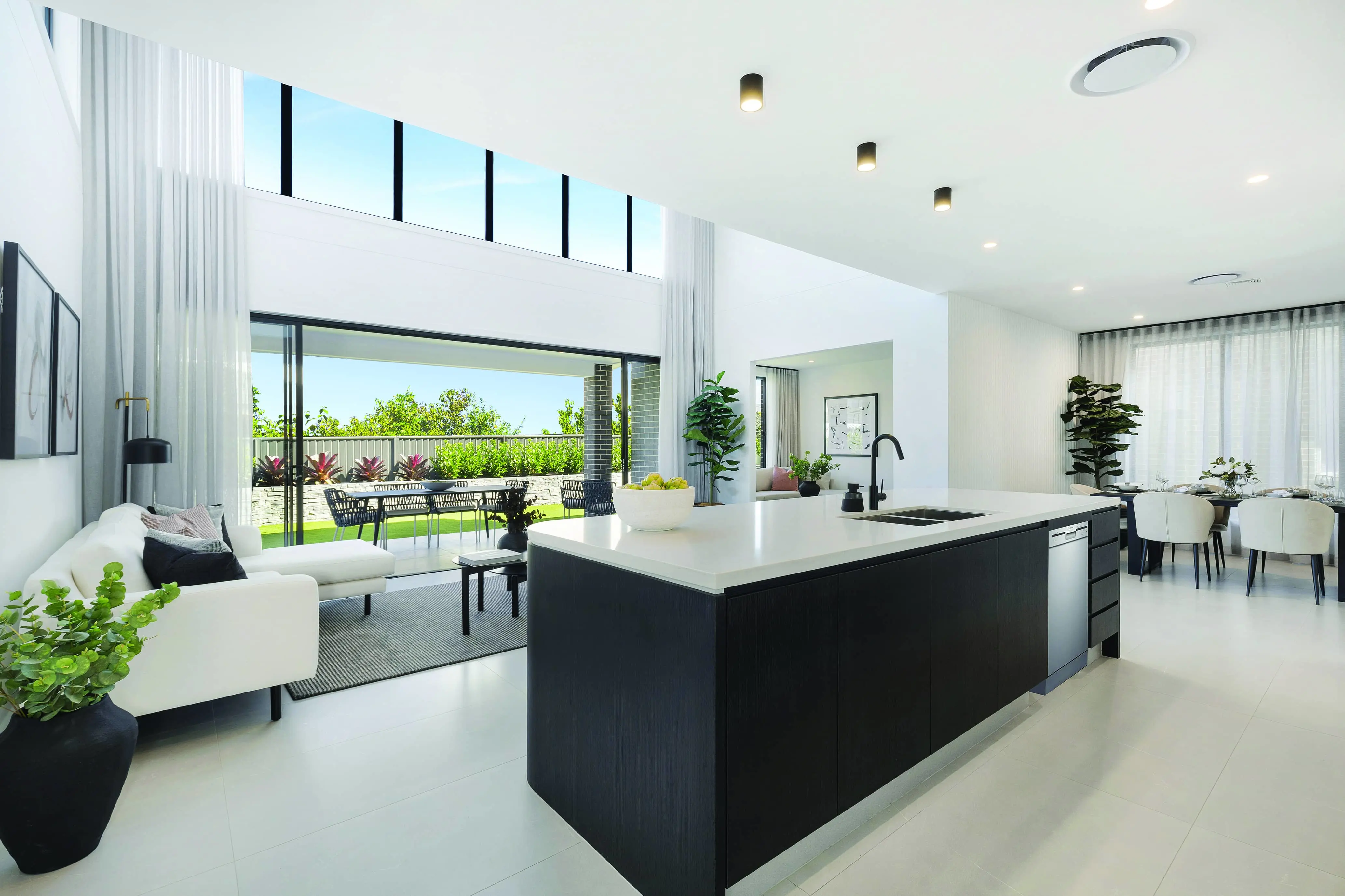 Modern open-concept kitchen and living area with black island, white countertops, and sliding doors opening to outdoor patio.