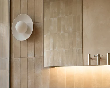 Modern bathroom with beige tiled walls, minimalist white wall sconce, and subtle under-cabinet lighting.