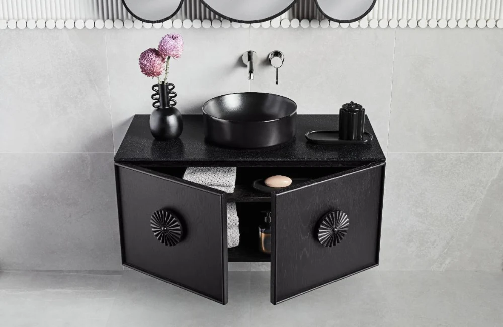 Modern black bathroom vanity with round vessel sink, wall-mounted faucet, and pink flowers in a small vase.