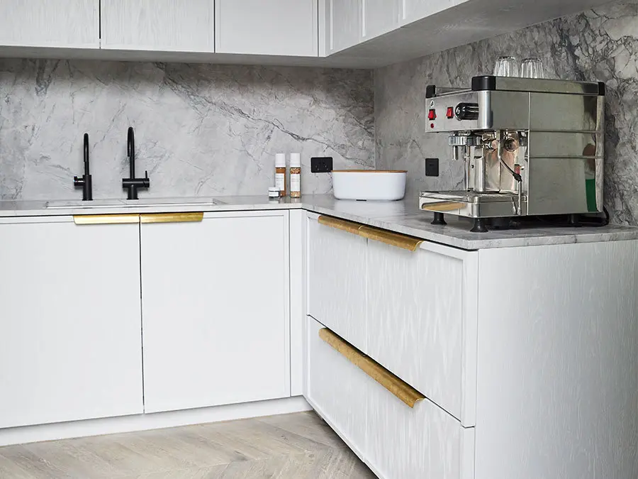 Modern white kitchen with marble backsplash, black faucet, and stainless steel espresso machine on countertop.