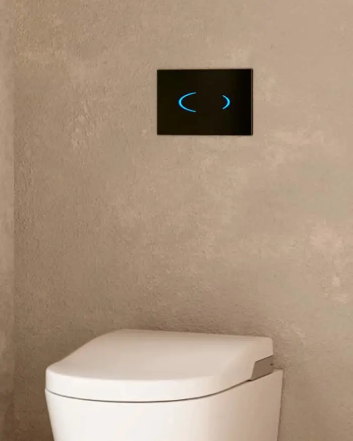 Modern white toilet with black wall panel featuring blue illuminated flush buttons mounted on beige wall.